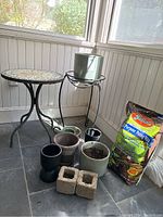 View of two round mosaic tables, multiple planters, and the potting soil bag in a sunroom area.