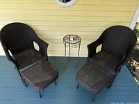 Two brown outdoor rattan chairs with matching ottomans placed on porch floor next to yellow siding wall.