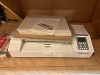 Front view of the Akiles ProLam Ultra-X6/XL laminator with operation manual and some laminate pouches on top.