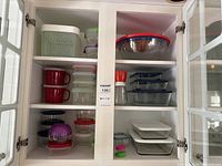 Full view of cupboard shelves holding assorted storage containers, mixing bowls, mugs, and lids.