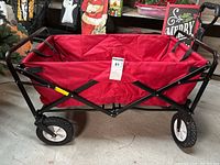 Side view of folding utility rolling cart showing red fabric and black metal frame with wheels and handle.