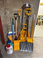 Photo of multiple snow shovels of different styles and handles, along with containers and bags of ice melt.
