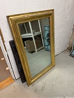 Large rectangular gold-framed mirror leaning against wall in basement