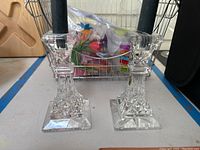 Photo showing two clear Waterford crystal candlestick holders with black taper candles on a table with a wire basket in background.