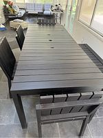 Full view of rectangular slatted dining table with center umbrella hole, four chairs and bench placed around table