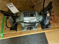 Overall view of the Delta 6 inch bench grinder showing the gray motor housing, black grinding wheels, side rests, and power switch.