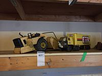 Yellow metal farm scraper and Home Hardware truck on wooden shelf showing rust and wear.