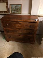 Front view of medium-dark brown wooden dresser with three drawers and round wooden knobs, showing wear.