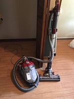 Full view of Dyson canister vacuum with hose and power head on wooden floor.