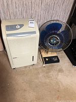 Lot showing the Danby dehumidifier positioned next to the blue desk fan on a floor against a wall.