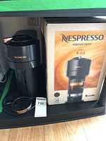 Photo of Nespresso Vertuo Next coffee machine in black with copper accents next to original retail box.