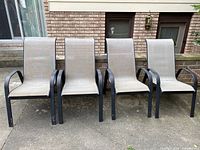 Four outdoor chairs with black metal frames and beige mesh seating shown in a row on a patio.