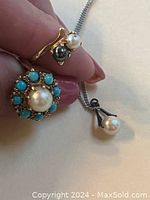 Hand holding two gold rings and a sterling silver necklace with pearl pendant arranged to show details of pearls and turquoise stones.