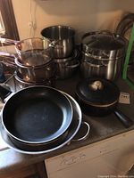 Photo showing a collection of stainless steel saucepans stacked together and two black frying pans in front.