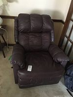 Full front view of the brown leatherette recliner rocker showing cushioned backrest, armrests, and seat, with a price tag attached to the seat area.