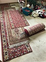 Four rug runners laid out with different lengths showing comprehensive patterns and fringes on ends. One runner is rolled and secured with metal rods.