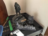 Soapstone sculptures group view showing hunter figure with seal on base, wolf sculptures, and the dog sled sculpture placed on a black crate.