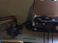 Two black metal Mission style outdoor light fixtures with glass panels on a table next to a Noma branded box and several plastic solar stake lights.