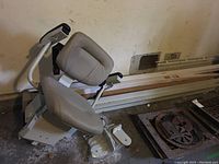 Side view of stair lift chair showing padded seat, armrests, and part of stair rail runner in background