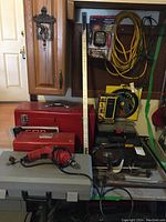 Overview of the tool lot showing large and small red toolboxes, electric drill, socket set, extension cord, clamps, pipe wrench, and jump-starting system.