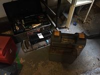 Photo showing three toolboxes: a black metal box with hand tools, a smaller black case, and a large gray plastic toolbox with compartments containing assorted hand tools and accessories.