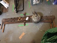 Top view of all items in the lot including two cross cut saws, a hand crank drill, an aluminum kettle, and a hand saw all placed on a concrete floor showing general wear and rust on the metal parts.