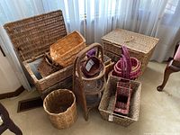 Photo showing an assortment of wicker baskets in various shapes, some stacked and arranged on carpeted floor near window.