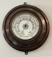 Front view showing carved wooden round frame and glass face with barometer dial.