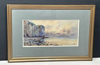 Full view of framed watercolour painting showing cliffs and rocky shore with muted color palette.