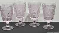 Front view of all four pink bunny pedestal water goblets lined up side by side on a dark surface; showing embossed bunny design and hobnail texture.