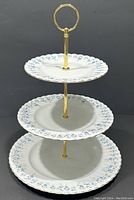 Front view showing the full three-tiered cake stand with blue floral china plates and gold-tone center rod and handle.