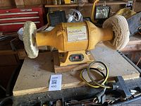 Front-side view of yellow Central Machinery buffer showing both buffing wheels and wooden base with power cord coiled around base.