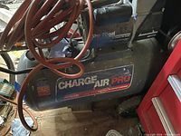Overall side view of Charge Air Pro air compressor with orange hose coiled on top and power motor visible