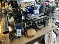 Side view of grey and black Delta Midi Lathe showing headstock, bed, tailstock, and tool rest assembled on workshop bench