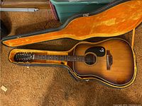 Full view of sunburst 12-string guitar seated in orange plush-lined hard shell case on carpet