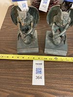Pair of gargoyle figurines from front showing size with measuring tape and labeled tags