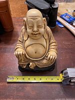 Front view of Buddha statue showing smiling face, hands resting on knees, large belly, and detailed robe with measuring tape indicating about 9 inches tall.