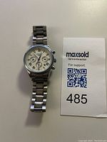 Full view of stainless steel Longines chronograph wristwatch laid next to MaxSold lot tag