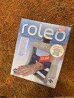 Front view of Roleo Pro Therapeutic Arm Massager box sealed in plastic wrap with branding and usage visuals.