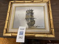 Full view of framed sailing ship painting with gold bamboo-style frame and linen mat.