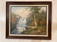 Framed oil painting of a waterfall in a natural setting with trees and mountains.