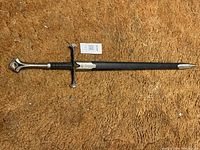 Full view of the sword sheathed on a brown carpet, showing the entire length and design.