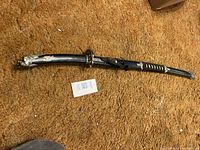 Full view of the black sword in its sheath laying on a brown carpet.