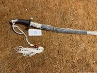 Full view of the sword showing black grip, metal guard, wrapped sheath, and white tassel with red bead.