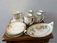 Entire set displayed on wooden surface showing five cups, five saucers, and tray with floral designs and gold trim