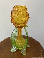 Close-up of amber and green vaseline glass decorative vase with flower-like form and stem base.