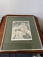Front view of framed artwork showing the print "Three Friends" with three stylized human figures. Silver metal frame with green matting.
