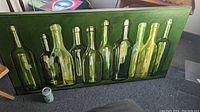 Frontal view of the oil painting showing the full row of green glass bottles with a dark green background.