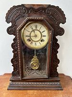 Front view of antique Ansonia gingerbread pendulum clock showing wooden carved case and octagonal clock face with Roman numerals.