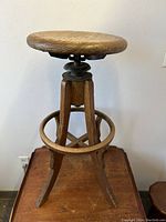 Front view of entire stool on wooden surface showing round seat, legs, and footring